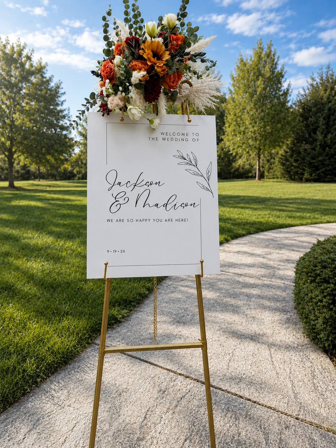 Fully styled wedding welcome easel outdoors with grass and a curved walkway